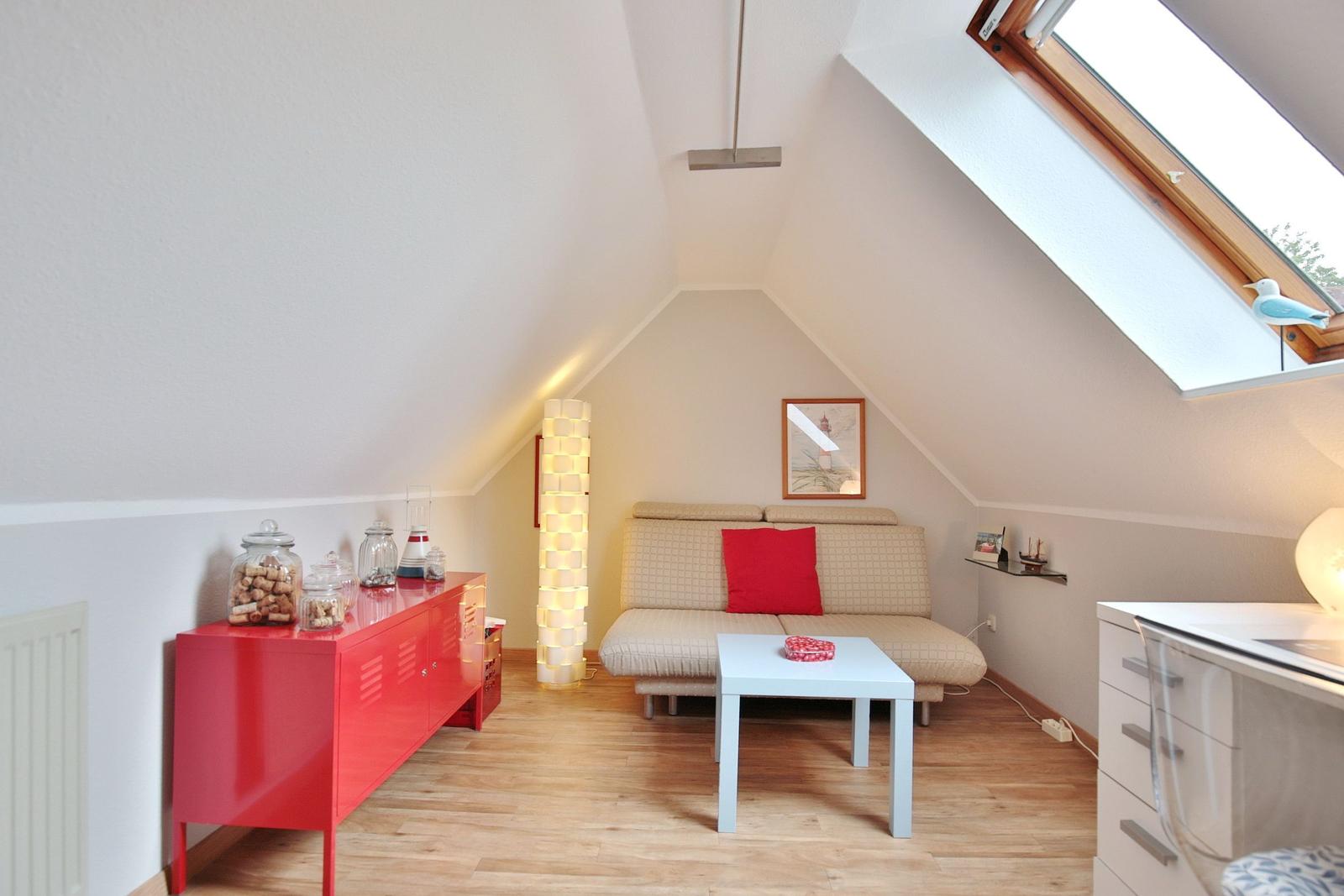 Attic room with sofa bed, table and red sideboard under sloped ceiling.