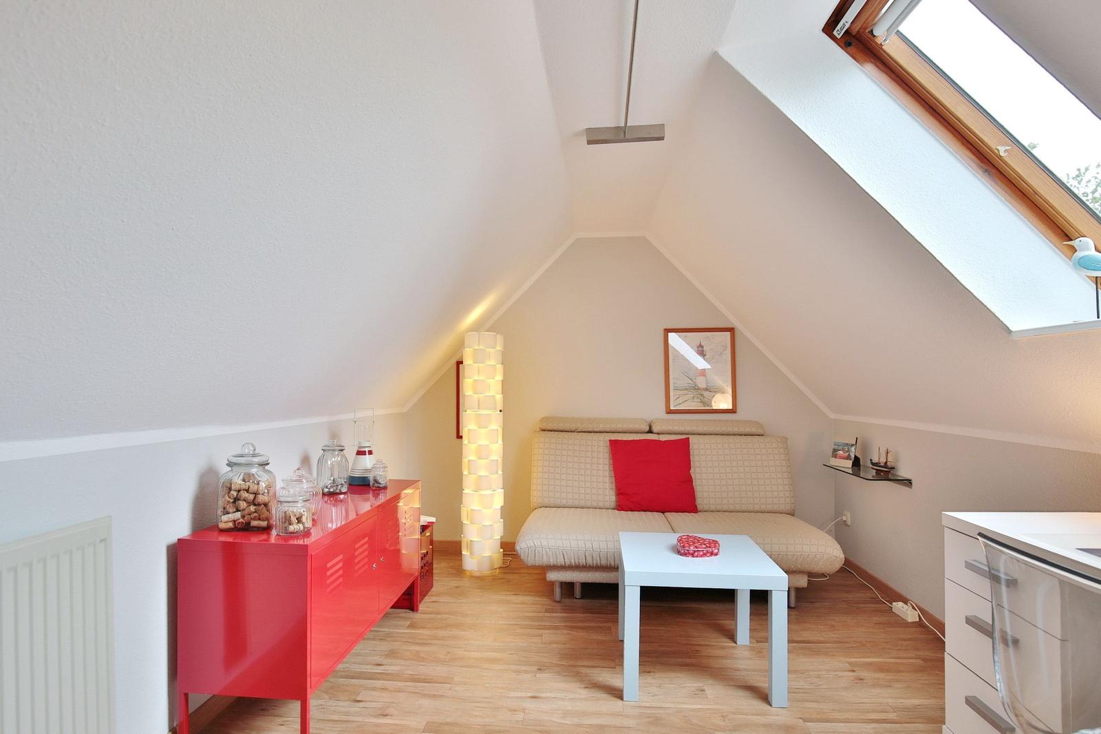 Attic room with sofa, table, and red sideboard under sloped ceiling.