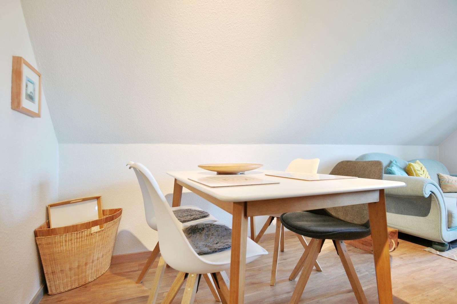 Dining area with table and chairs, sofa in background, basket on wall.