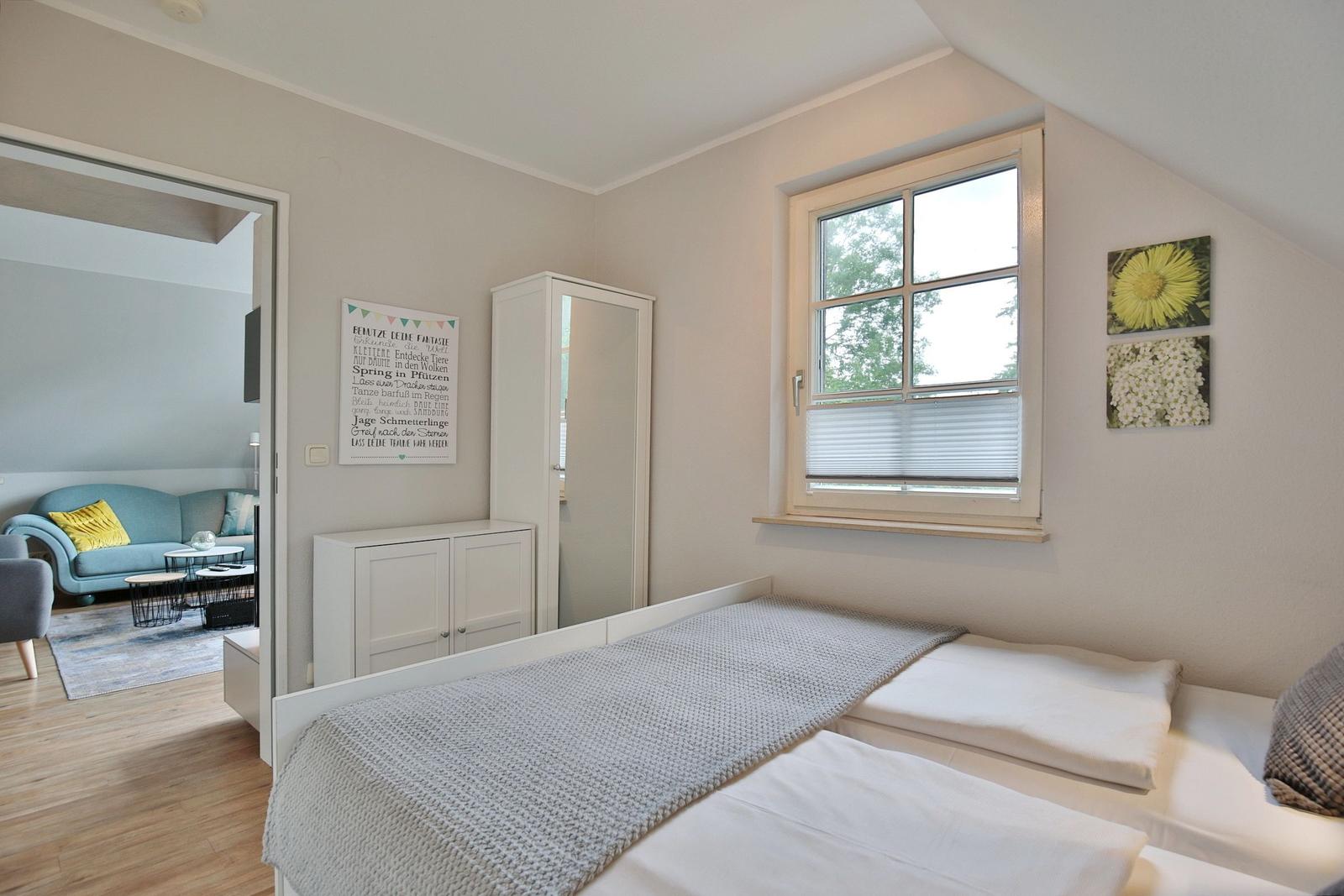 Bedroom with double bed, window, and view into living area with sofa.