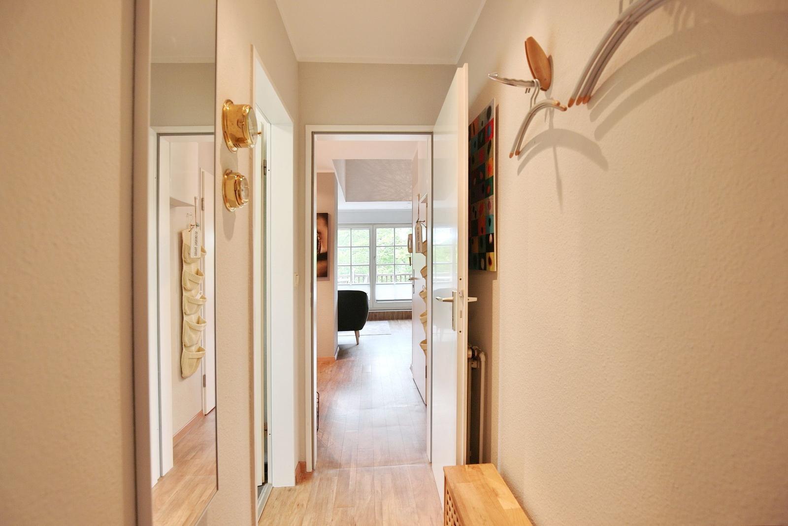 Hallway with doorways, wall art, and wooden floor. View into living area with window.