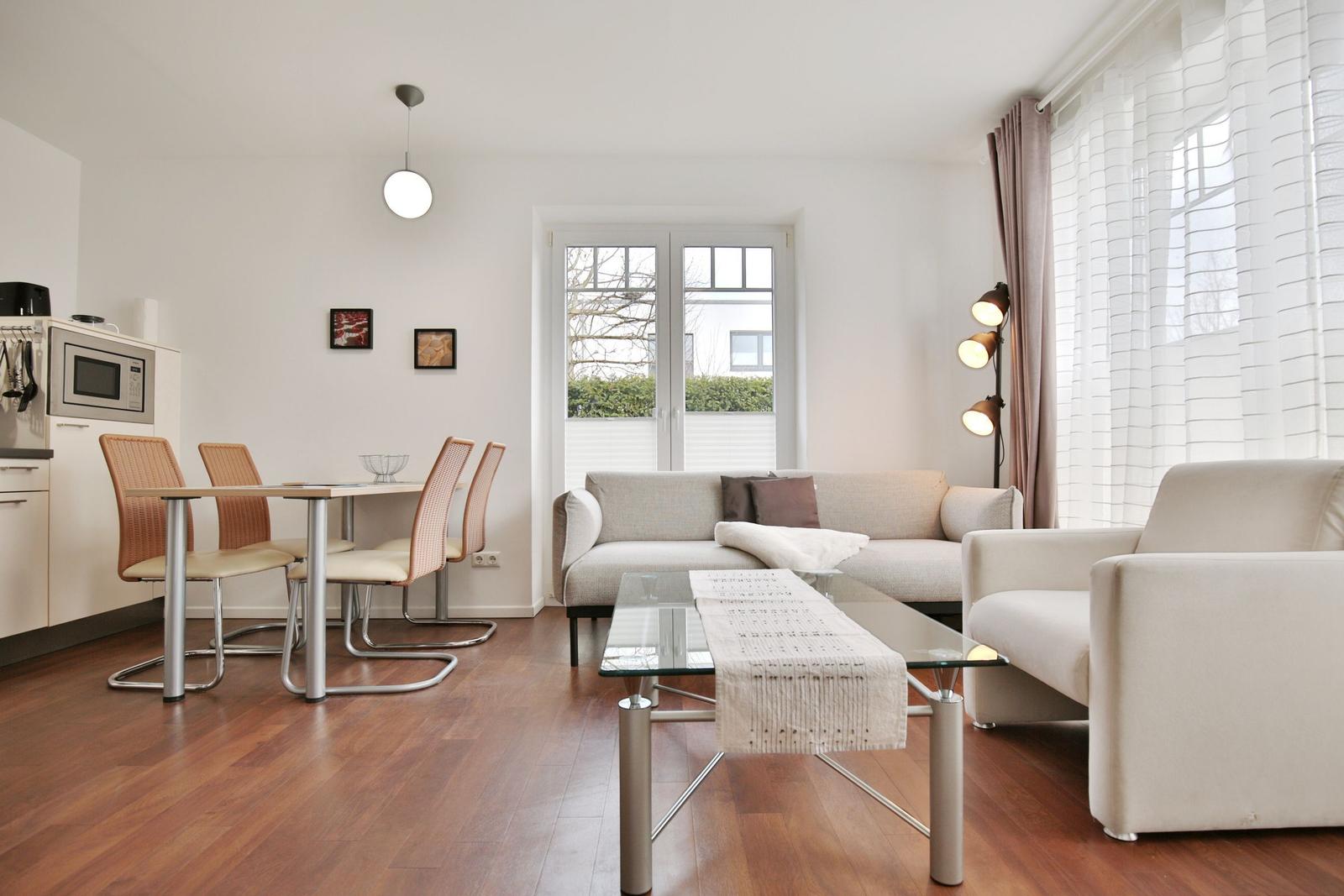 Wohn- und Essbereich mit Sofa, Sitzbank, Glas-Tisch und Küchenzeile.