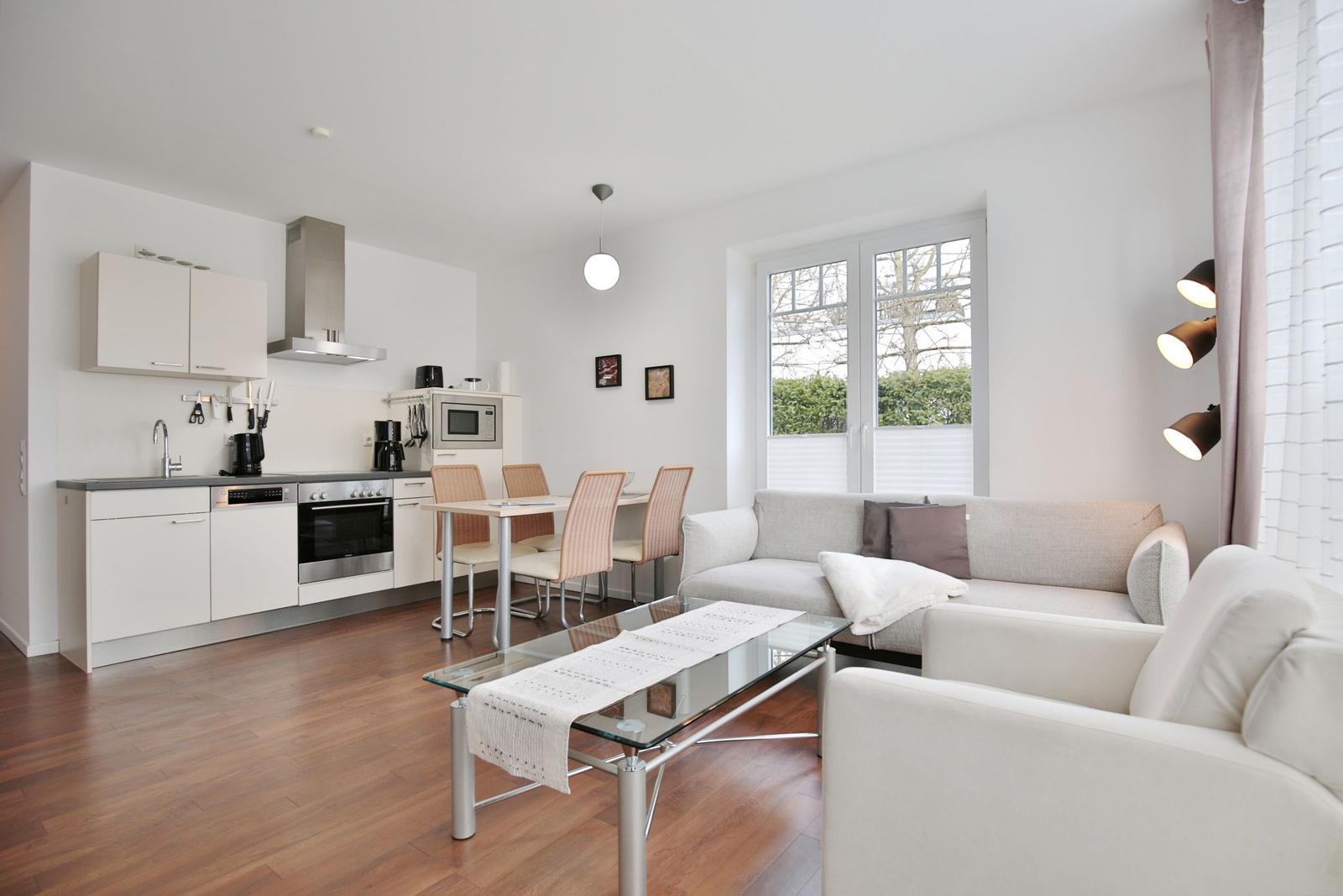 Wohnküche mit Essbereich, Sofa und Glas-Tisch. Holzboden und Fenster mit Blick.