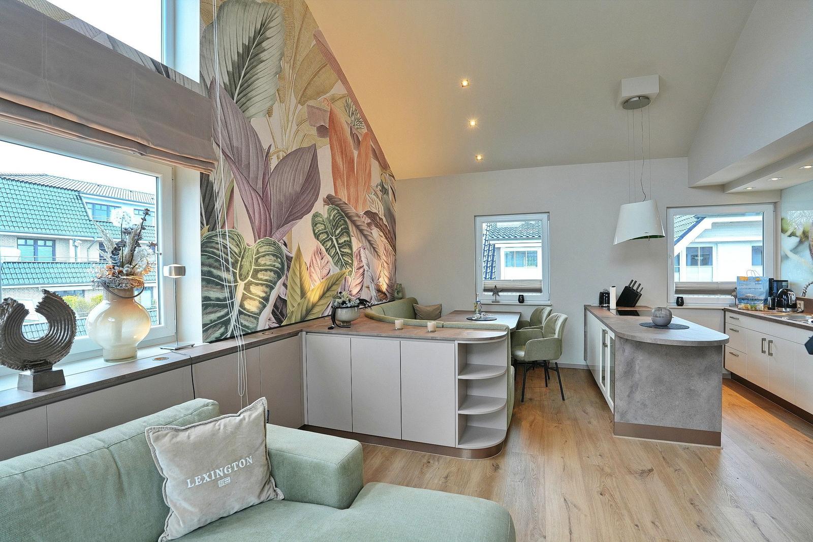 Living and kitchen area with large windows, wallpaper, and kitchen island.
