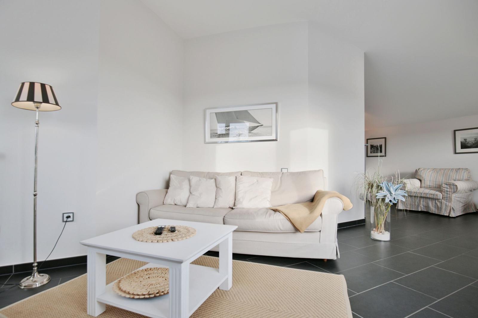 Wohnzimmer mit Sofa, Tisch und Stehlampe. Hintergrund zeigt einen weiteren Sitzbereich.