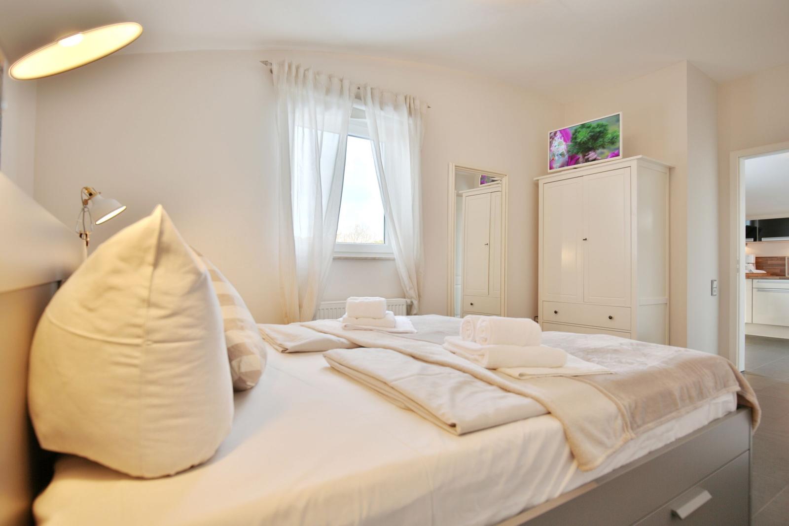 Schlafzimmer mit Bett, Kleiderschrank und Fenster. Auf dem Bett liegen Handtücher.