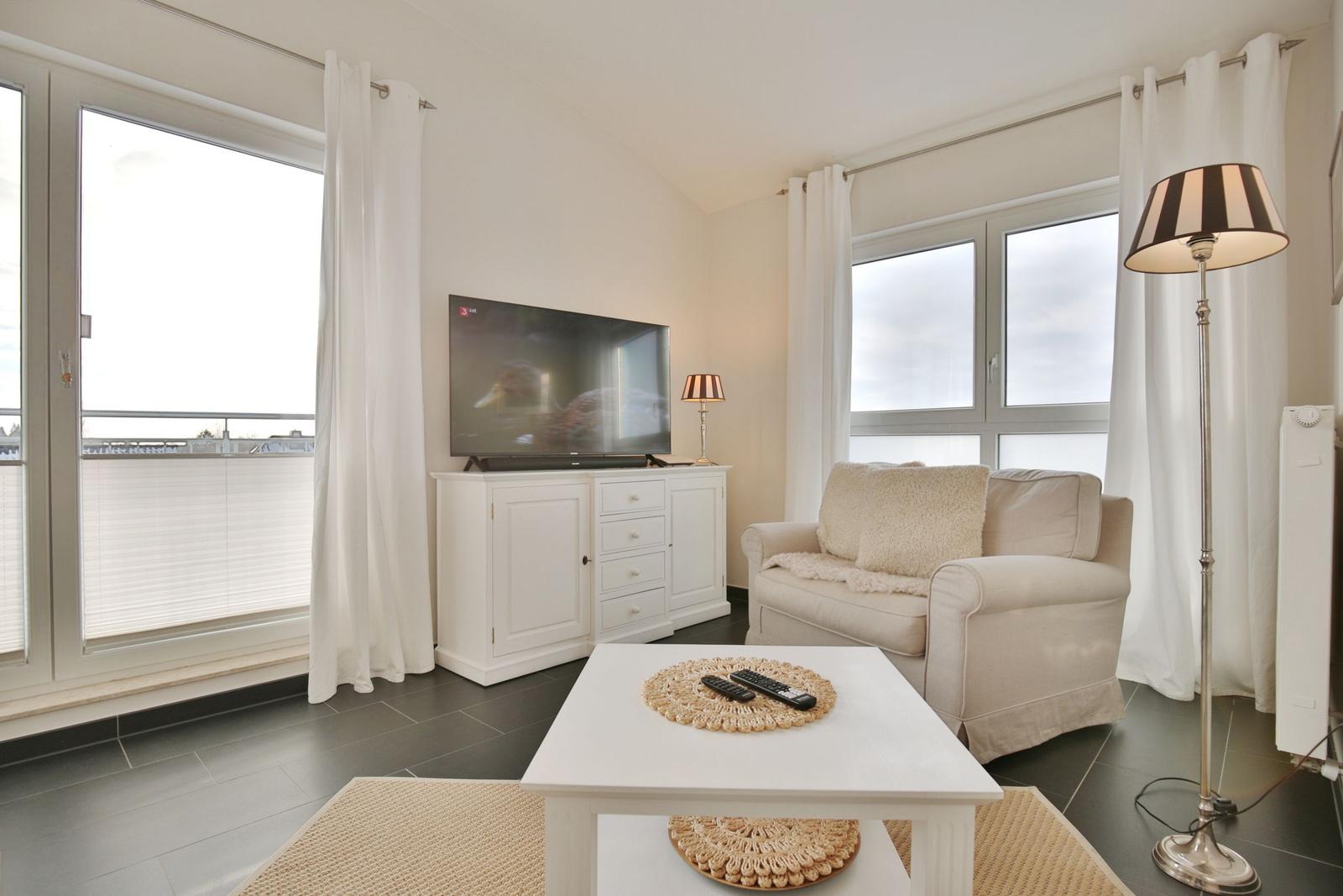 Wohnzimmer mit Sofa, Fernseher und großem Fenster mit Blick auf Balkon.