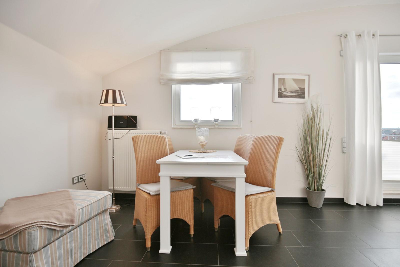 Essbereich mit weißem Tisch, vier Stühlen und Fenster. Nebenher Sofa und Pflanze.