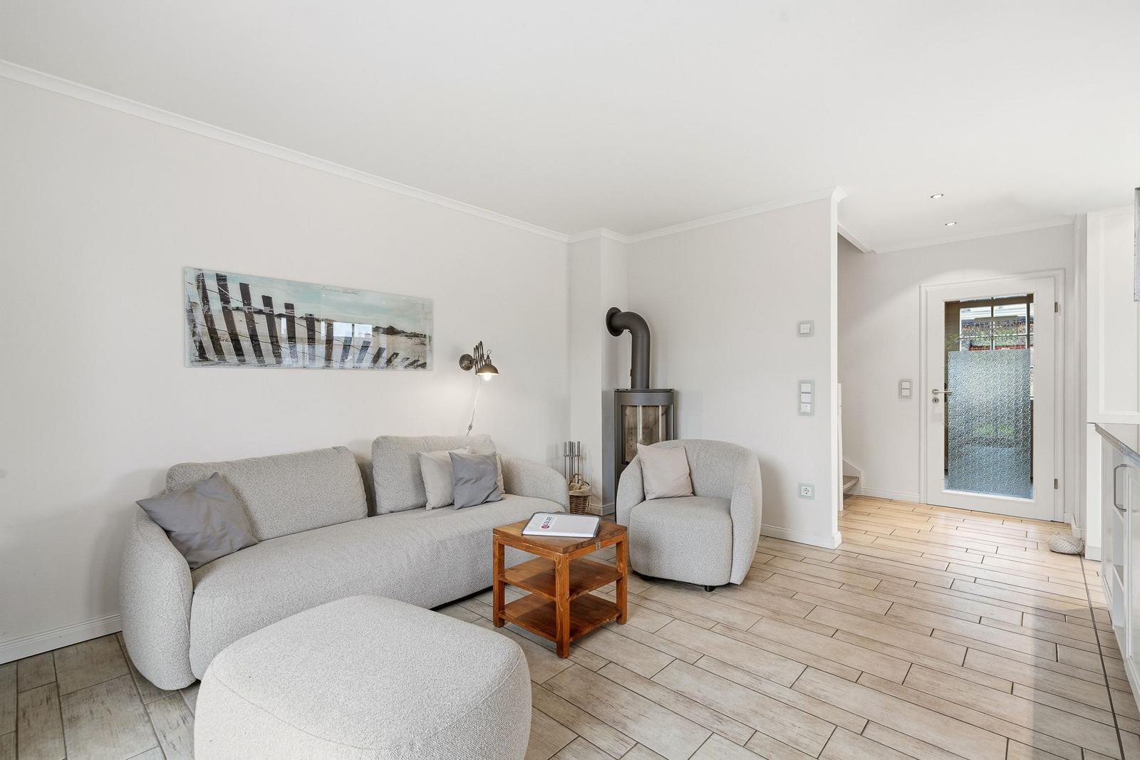 Wohnzimmer mit Sofa, Sessel und Kaminofen. Holzfußboden und Wandbild.