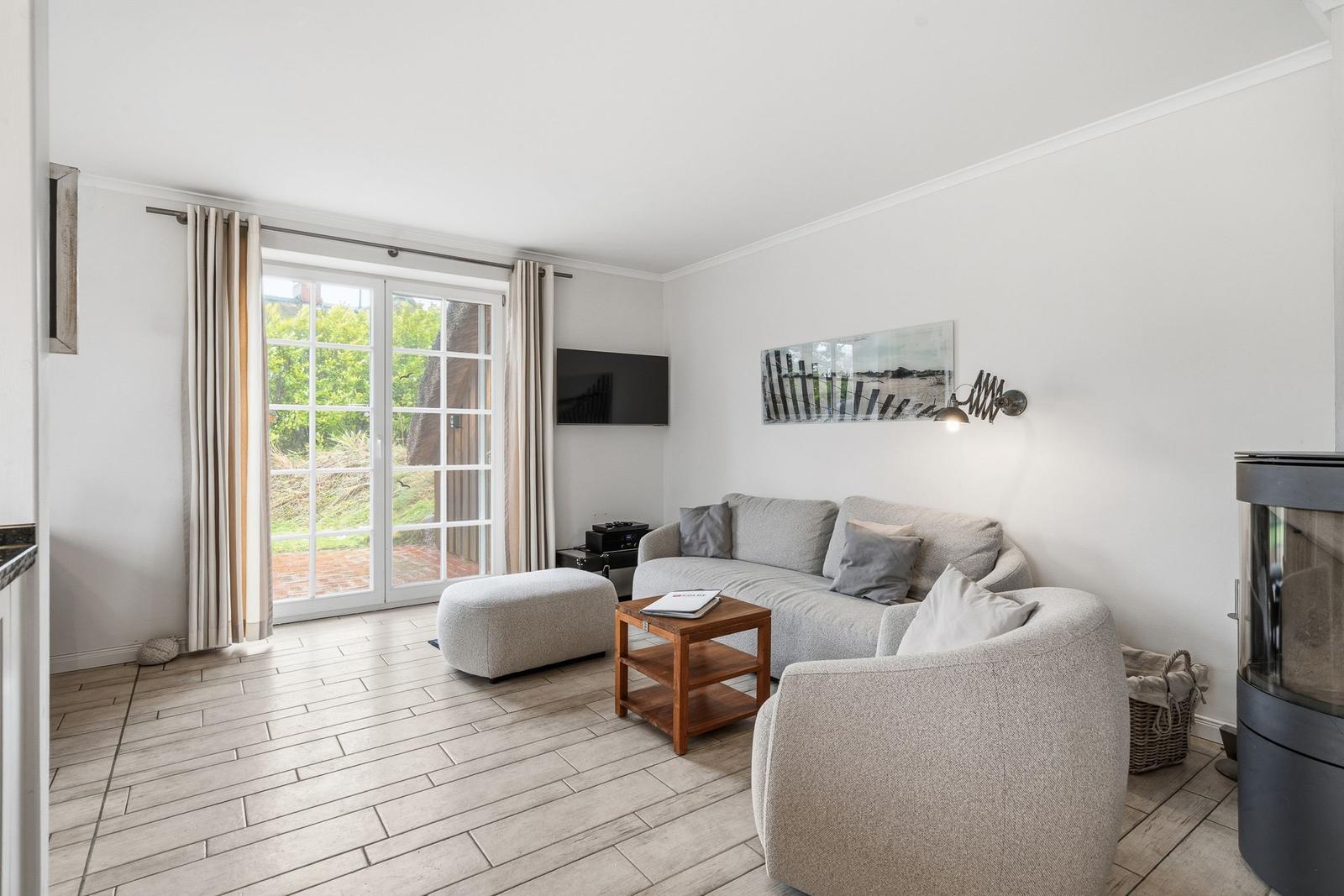 Wohnzimmer mit Sofa, Sessel, TV und Glasfront zur Terrasse.