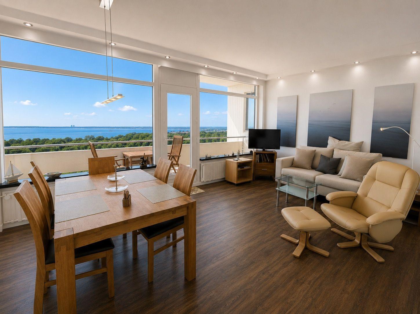 Living and dining area with view of water and greenery. Wooden table, sofa, and chair.