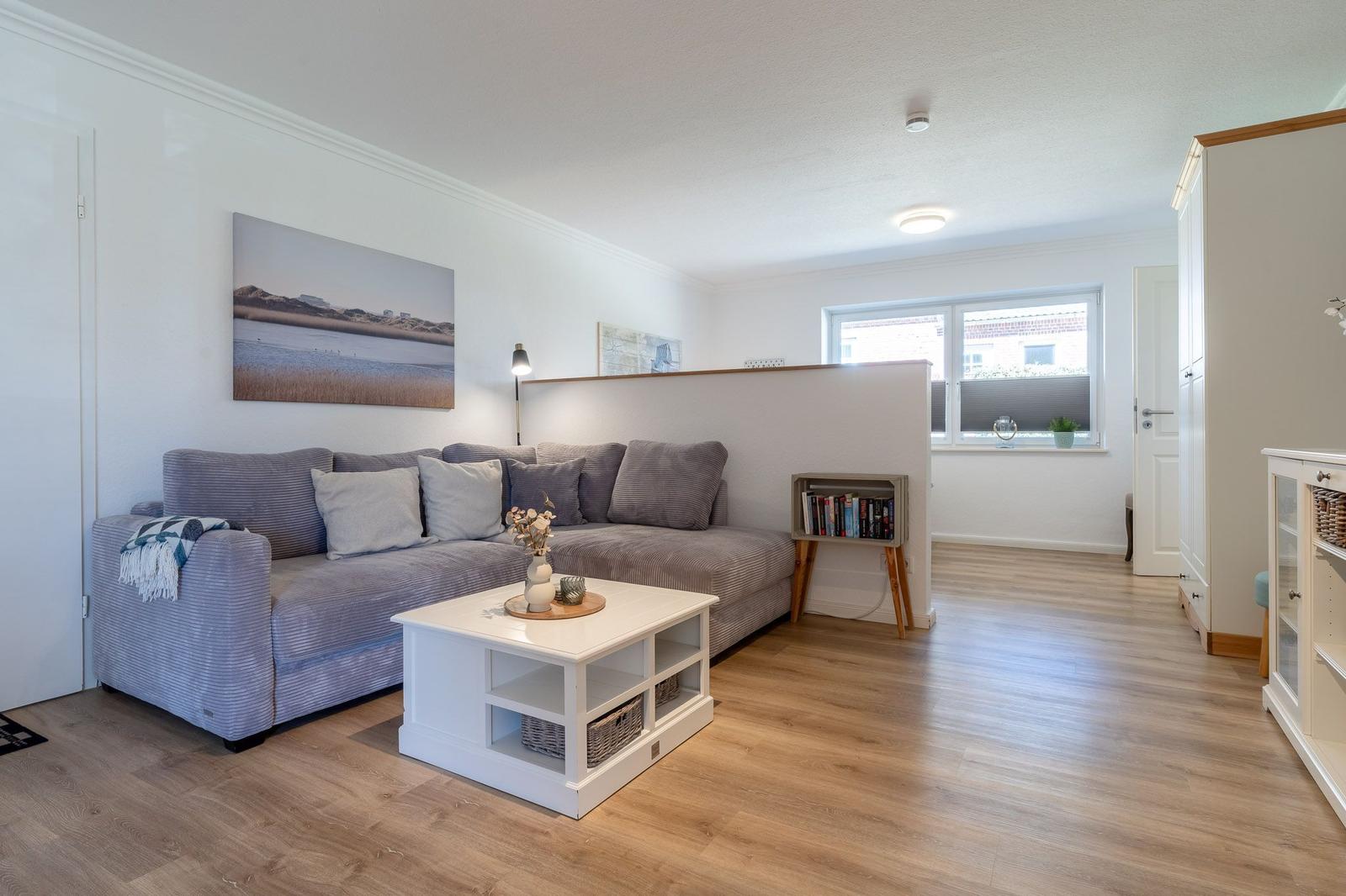 Wohnzimmer mit grauem Sofa, weißem Couchtisch und Holzboden. An der Wand hängt ein großes Bild.