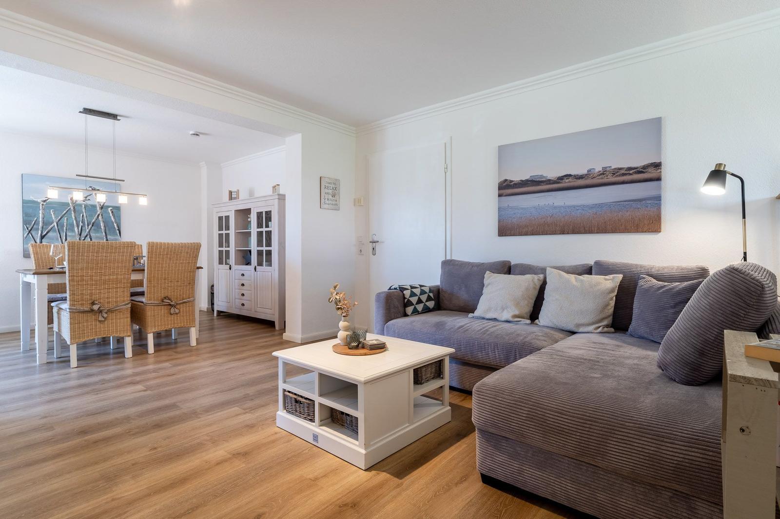Wohn- und Essbereich mit grauem Sofa, weißem Couchtisch und Holzboden.