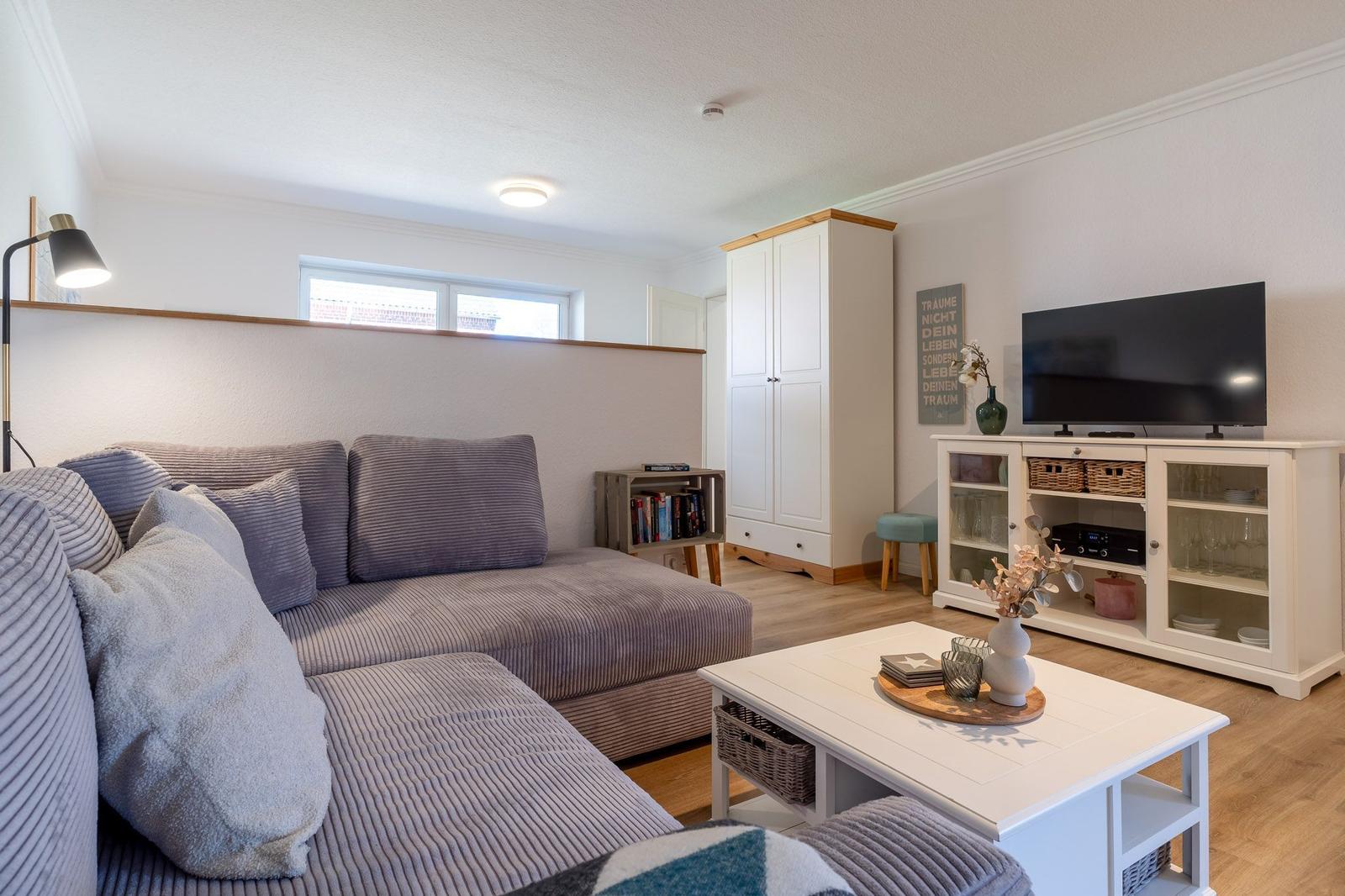 Wohnzimmer mit Sofa, Couchtisch und TV-Schrank. Holzboden und Fenster.