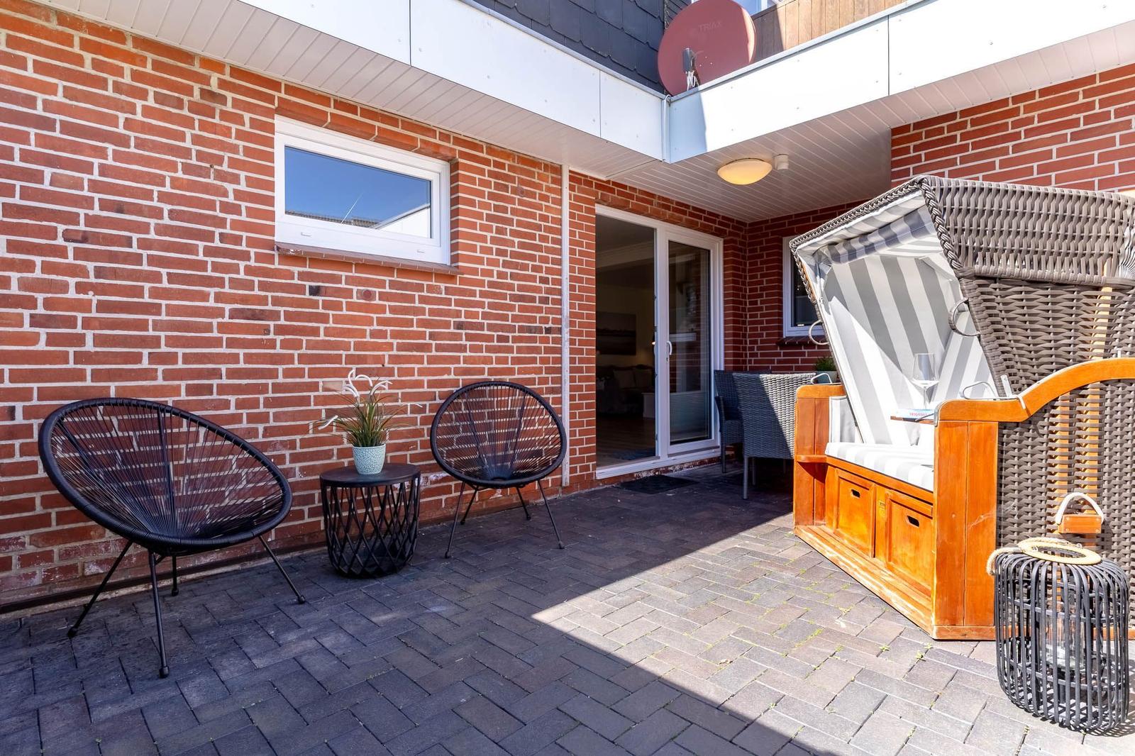 Terrasse mit zwei Sesseln, Tisch, Liegestuhl und Pflanze vor rotem Backsteinhaus.
