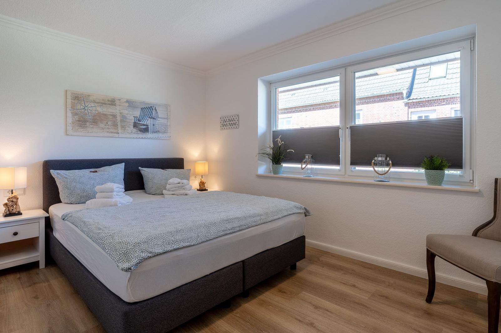 Schlafzimmer mit Bett, Nachttisch, Fenster und Stuhl.