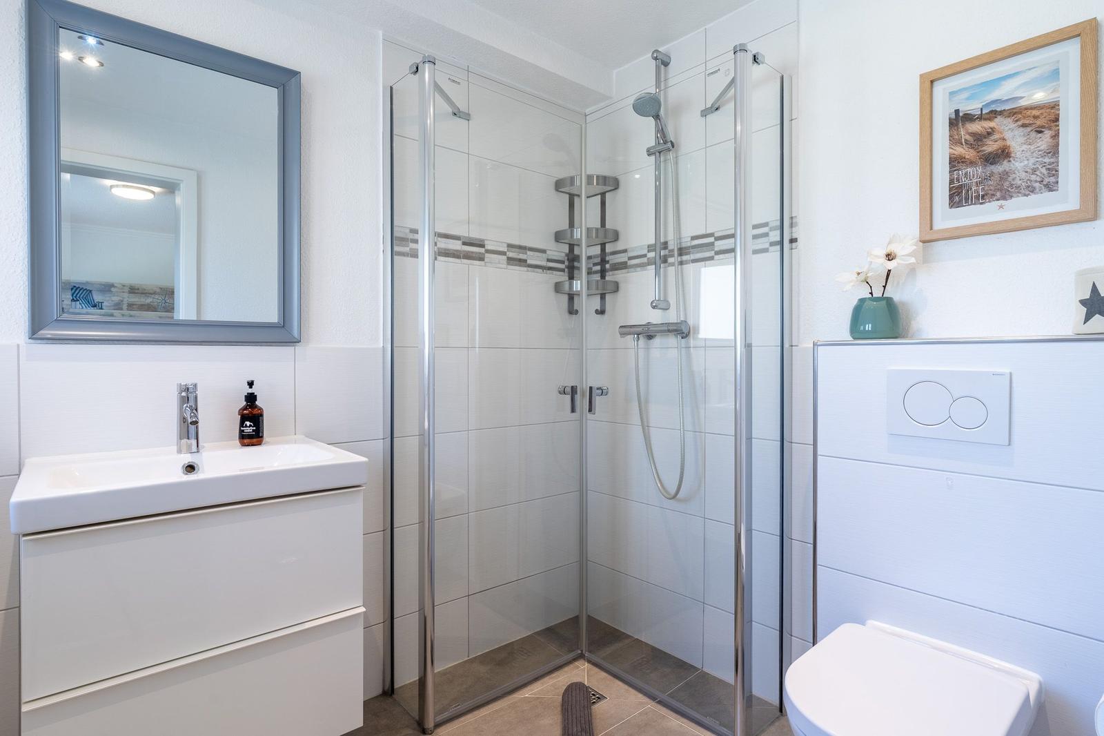 Badezimmer mit Dusche, Waschbecken und Toilette. Fliesen und moderne Einrichtung.