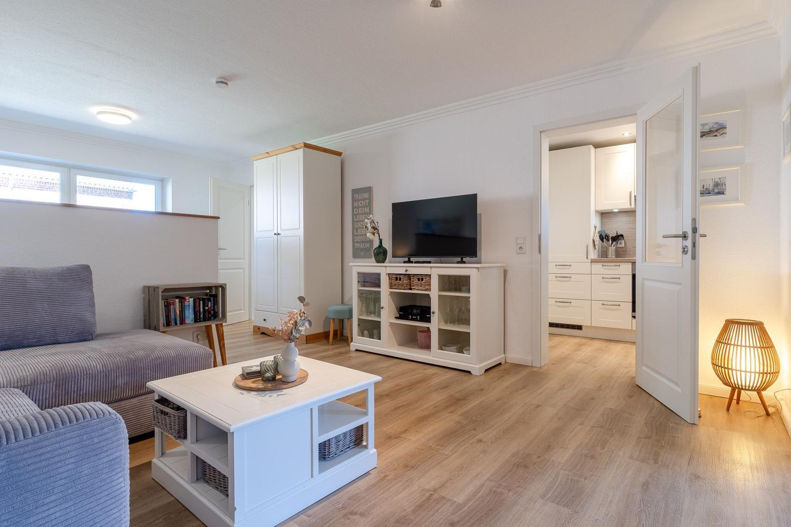 Wohnzimmer mit Sofa, Couchtisch und TV. Küche im Hintergrund sichtbar.