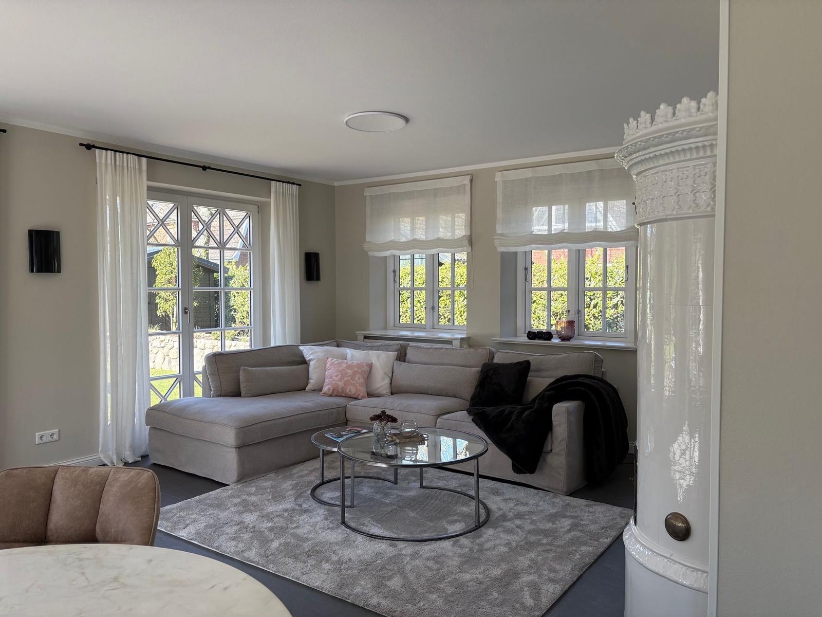 Wohnzimmer mit großem Sofa, Glas-Tisch und Fenstern zum Garten.