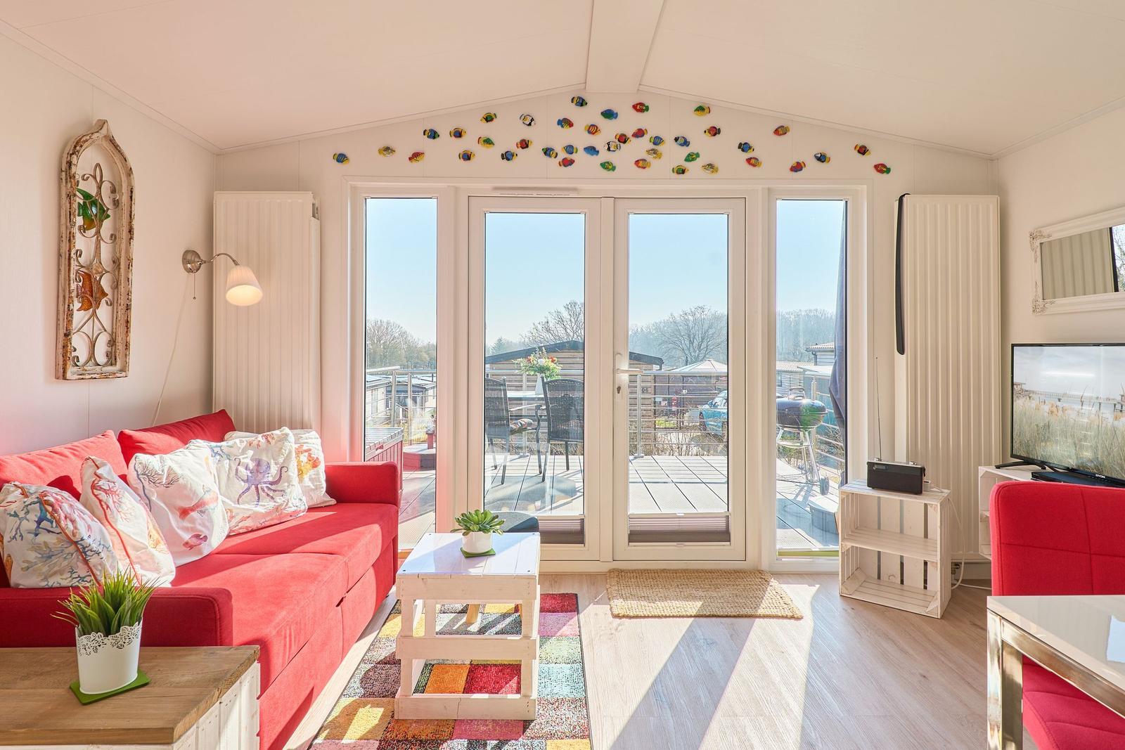 Ein Wohnraum mit rotem Sofa, Glasfront und Terrasse im Hintergrund.