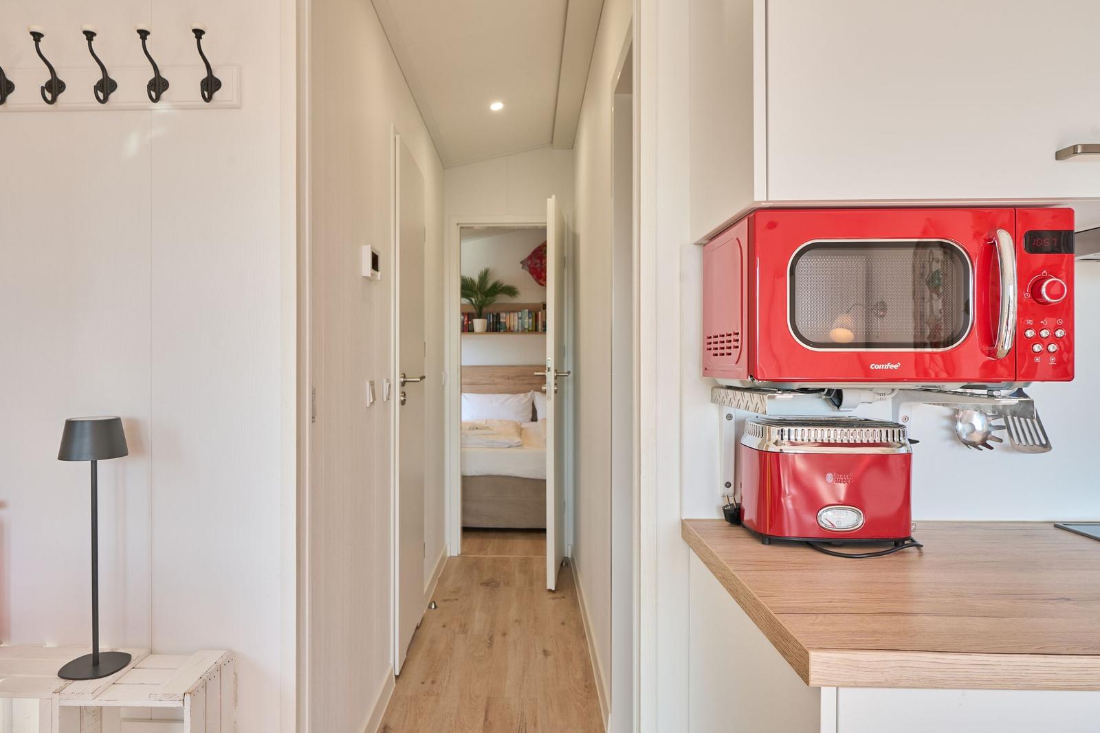 Küche mit rotem Mikrowellenherd und Toaster. Flur führt zum Schlafzimmer mit Bett und Bücherregal.