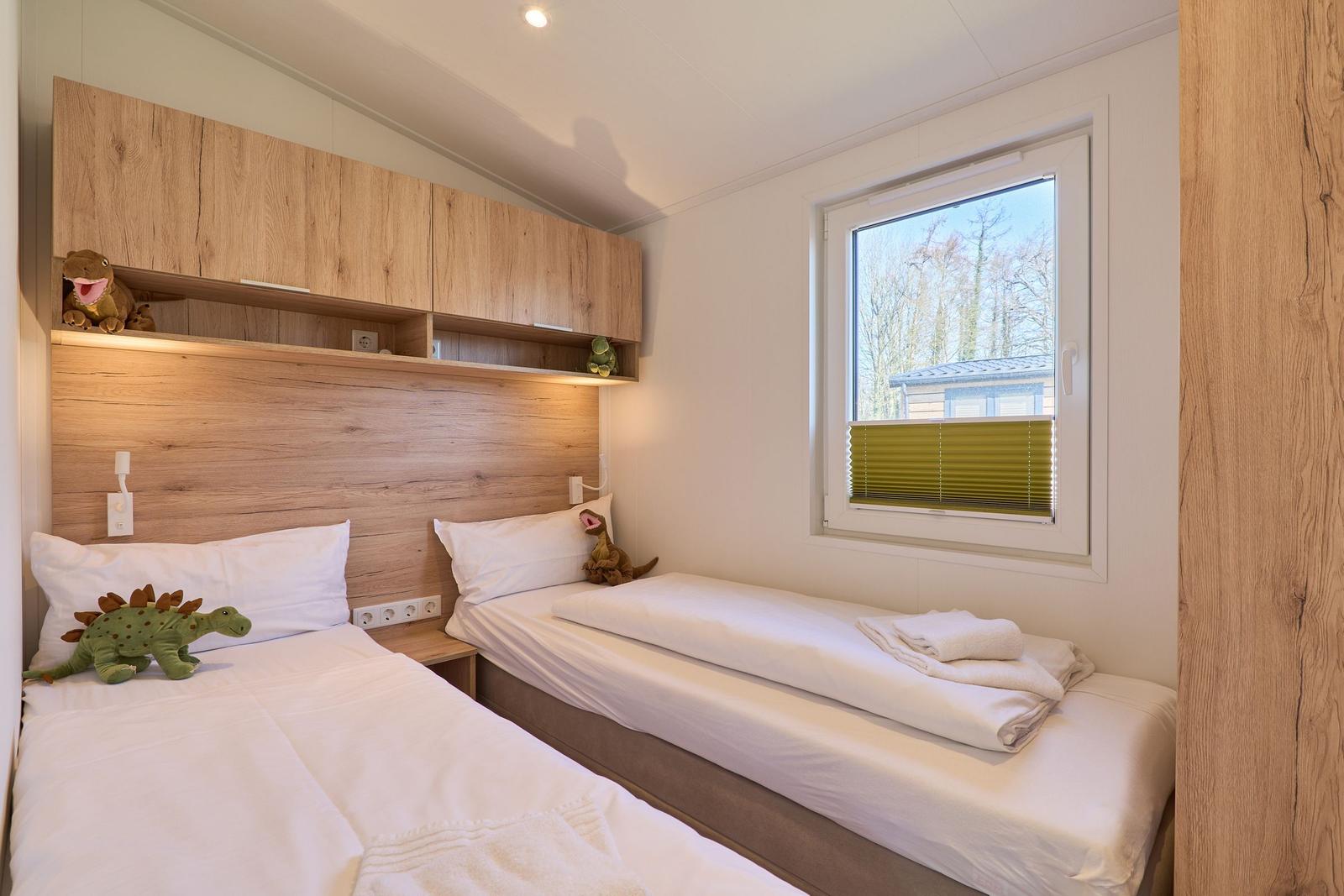 Zwei Einzelbetten mit weißen Bettwäsche, Holzregal und Fenster mit Blick auf Bäume.