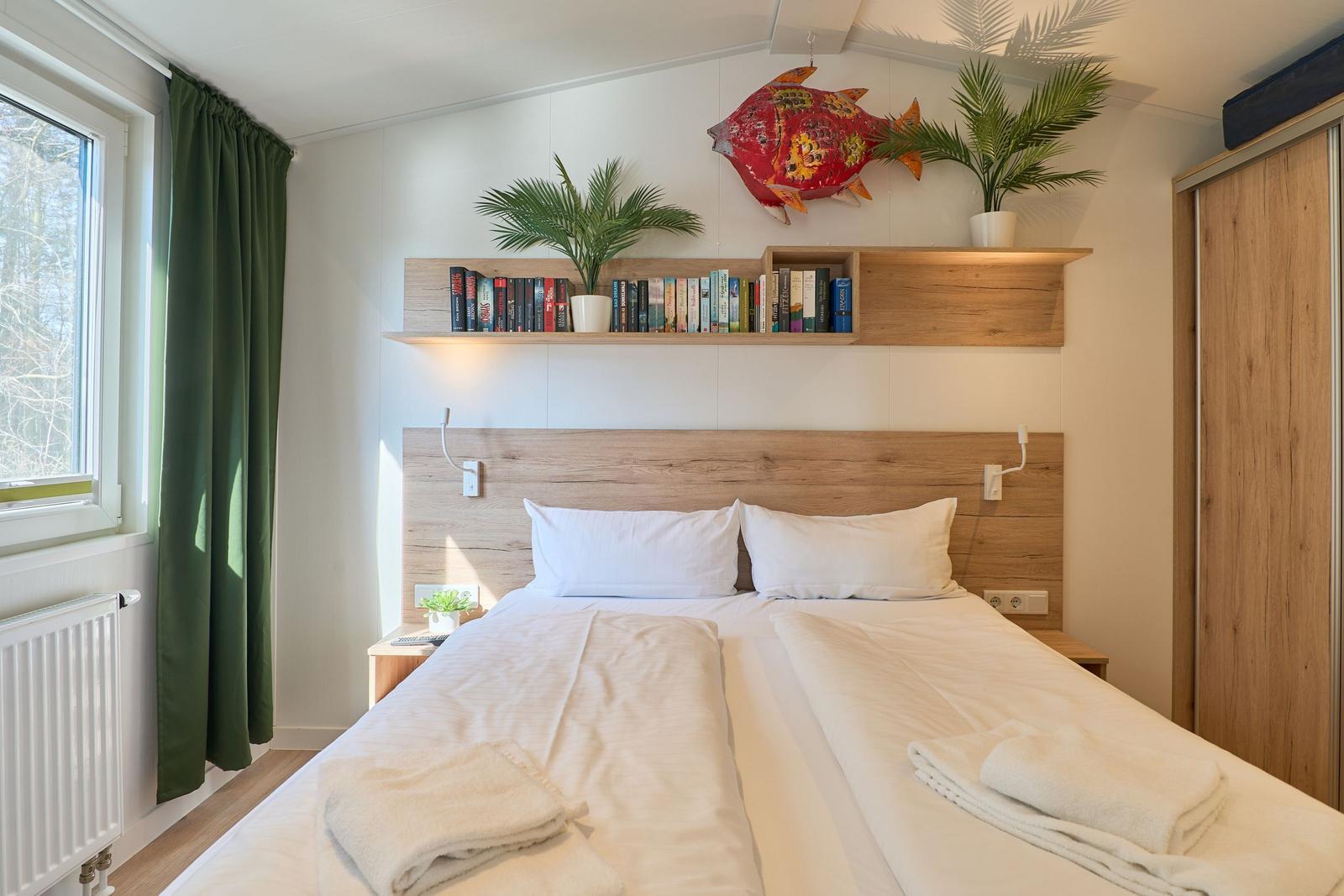 Schlafzimmer mit Doppelbett, Bücherregal und Pflanzen an der Wand.