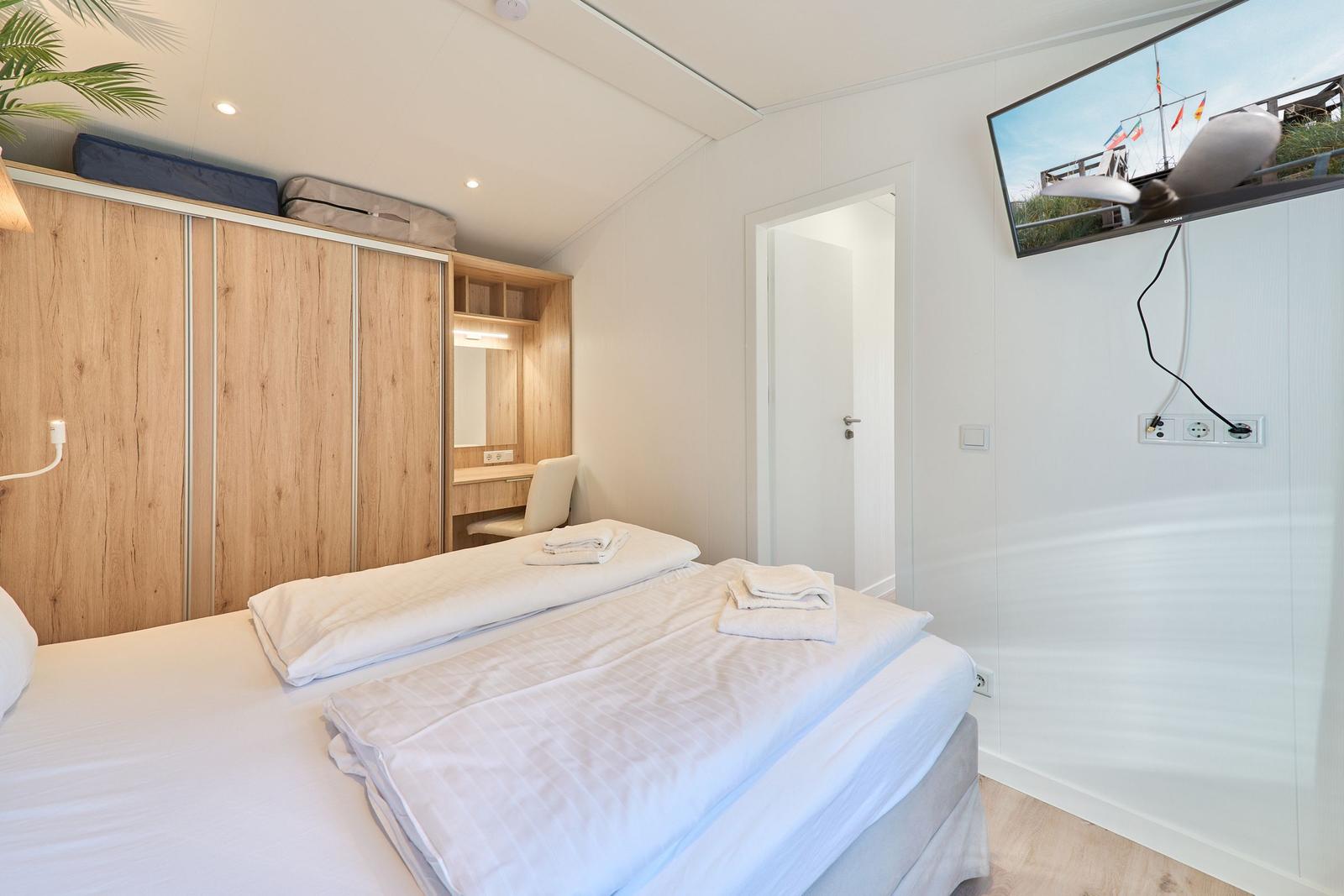 Schlafzimmer mit Bett, Kleiderschrank und Fernseher an der Wand.