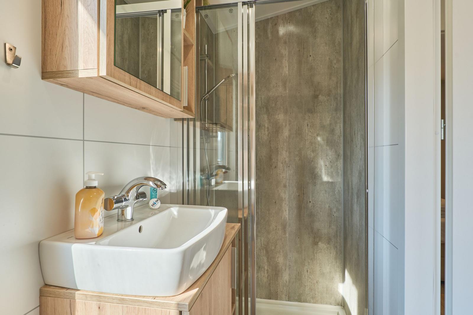 Bad mit Dusche, Waschbecken und Holzschränken.