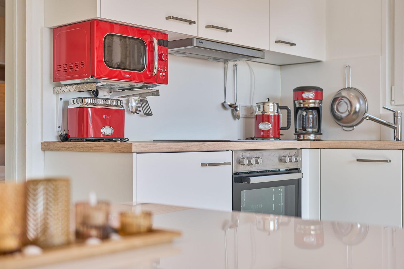 Küche mit rotem Mikrowellenherd, Toaster und Kaffeemaschine. Weiße Schränke und Holzoberfläche.