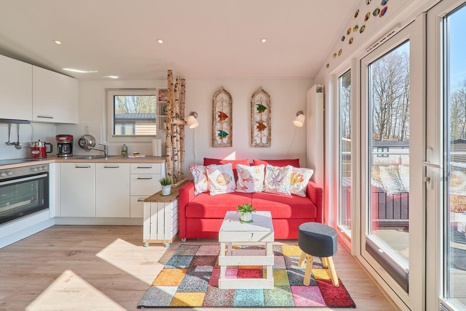 Ein Wohnbereich mit rotem Sofa, Küchenzeile und großem Fenster.