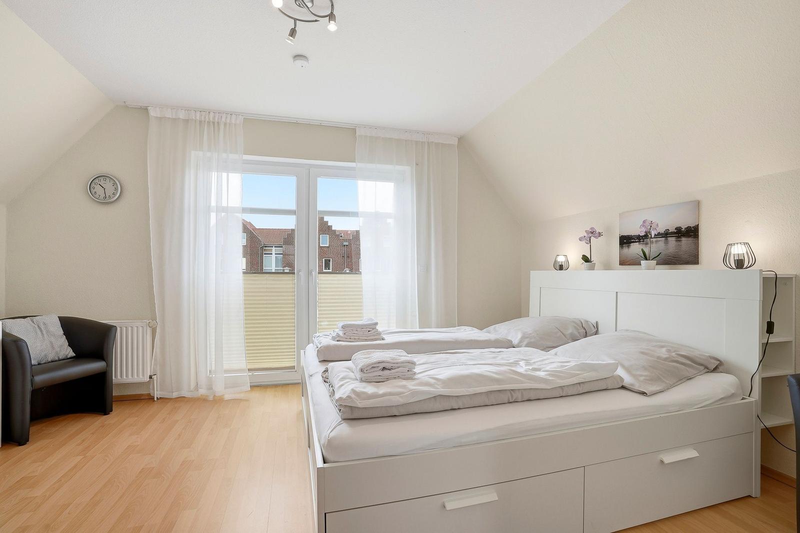 Schlafzimmer mit Doppelbett, Fenster und Sitzgelegenheit.