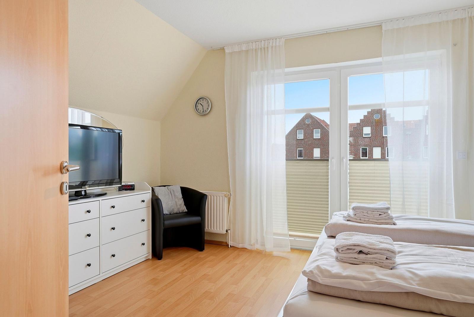 Schlafzimmer mit Doppelbett, TV und Sicht auf Gebäude durch Glastür.