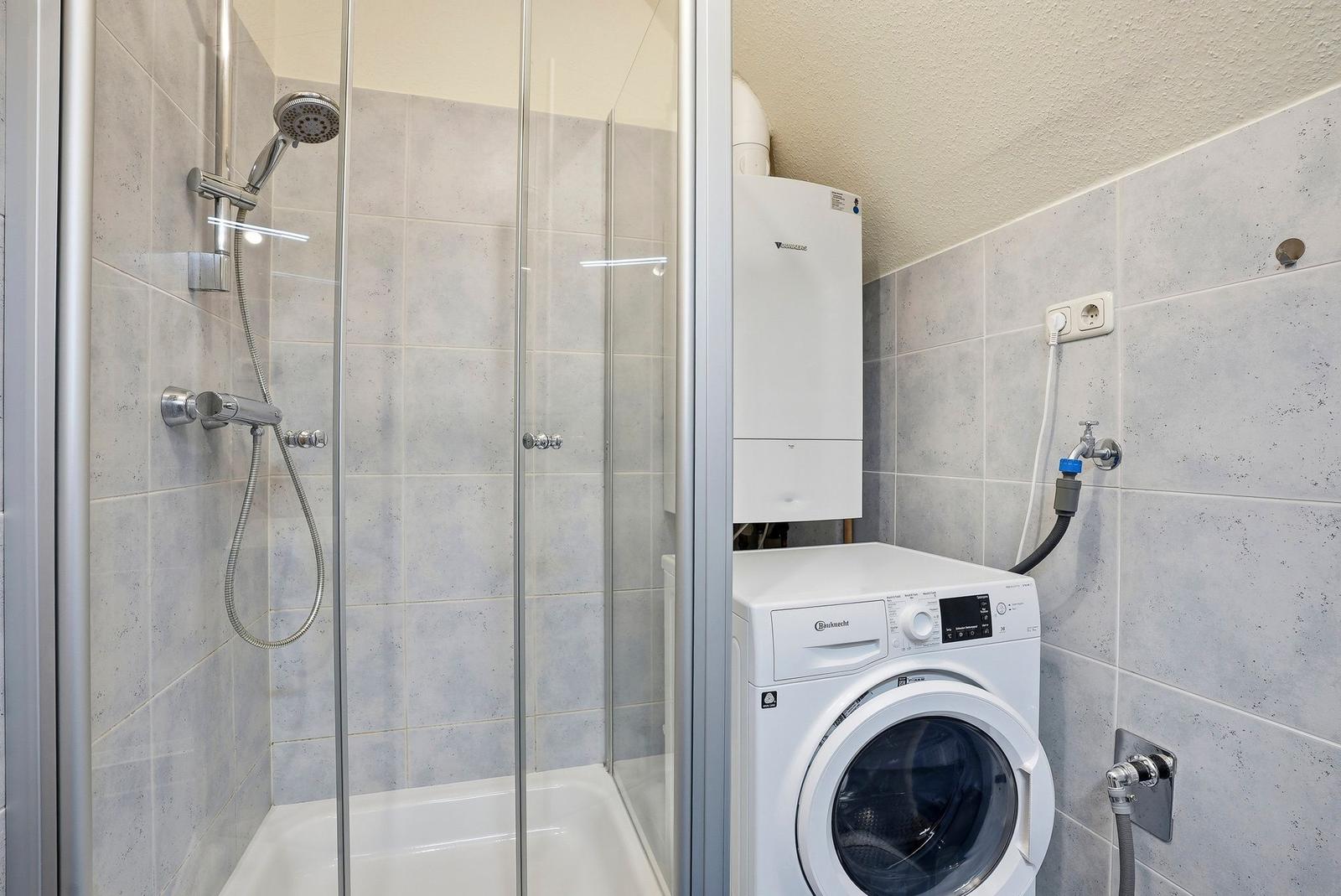 Dusche mit Glaswand, Waschmaschine und Heizung in Badezimmer