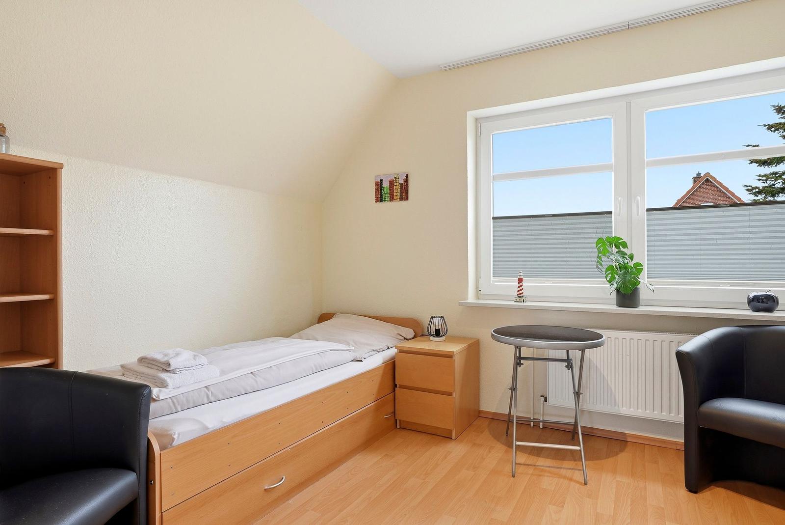 Schlafzimmer mit Doppelbett, Schreibtisch und Fenster mit Blick auf Garten.