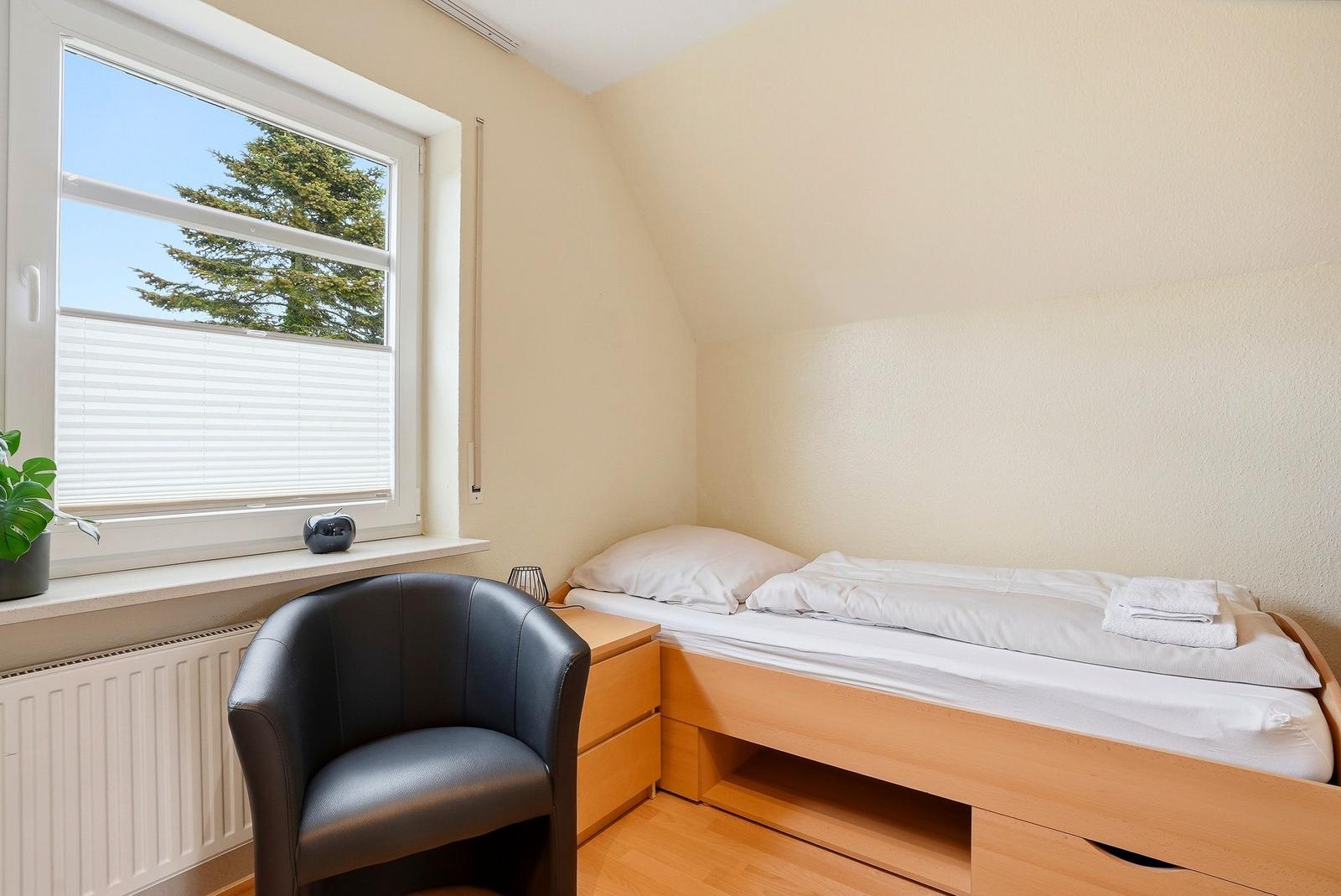 Ein Schlafzimmer mit einem Bett, einem Stuhl und einem Fenster mit Blick auf einen Baum.