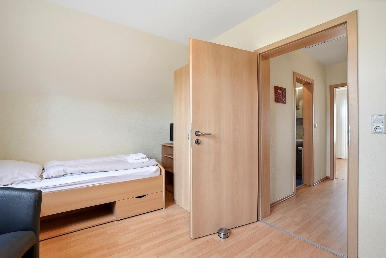 Schlafzimmer mit Bett, Schrank und Tür zum Flur. Holzfußboden und neutrale Wände.