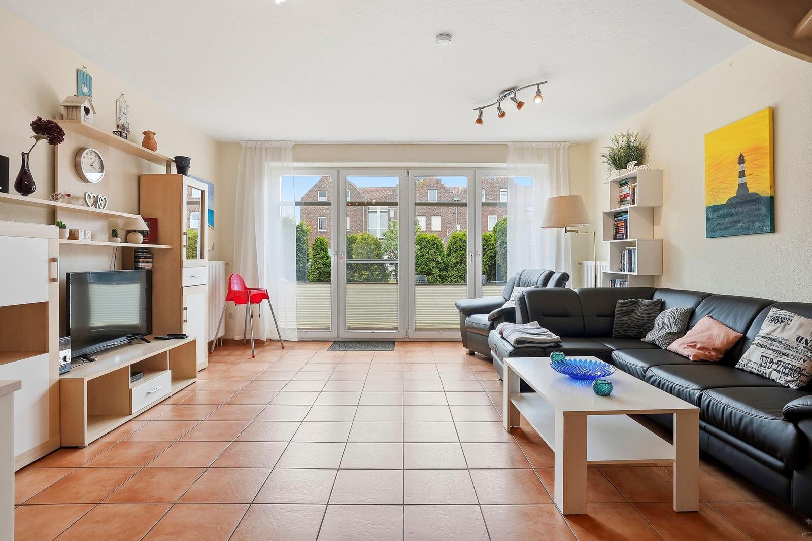 Wohnzimmer mit Sofa, Couchtisch und TV. Durchgang zur Terrasse mit Blick auf Grünflächen.