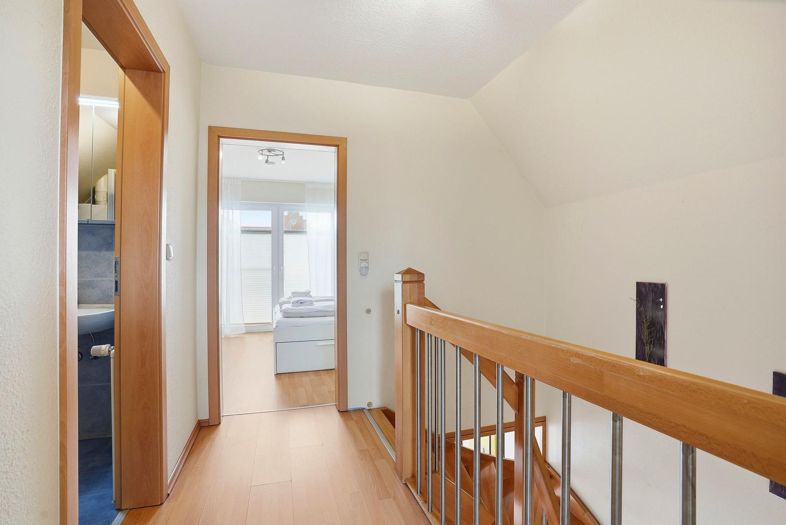 Flur mit Holztreppe, Schlafzimmer und Badezimmer im Hintergrund.