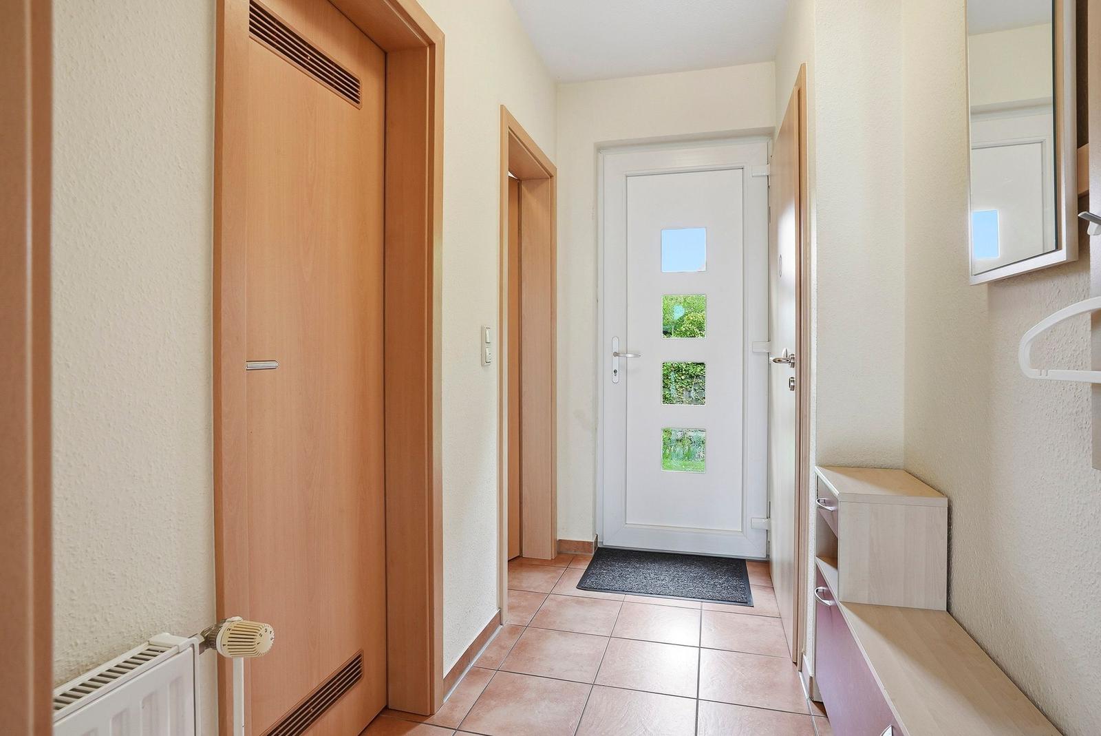 Flur mit Holztüren, Fliesenboden und Spiegelschrank an der Wand.