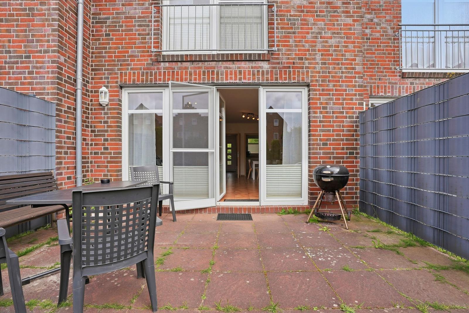 Hinterhof mit Terrasse, Grill und Tisch. Durchgang zur Wohnung.