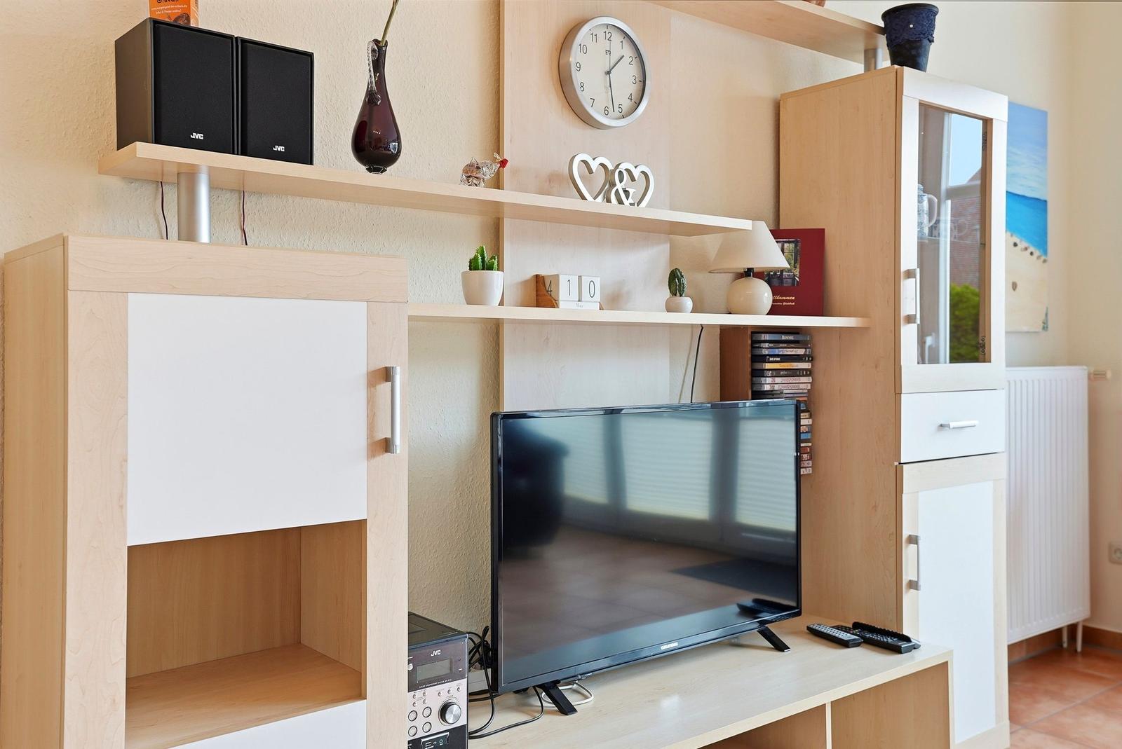 TV-Gerät auf Holzregal mit Uhr, Pflanzen und Dekoration.