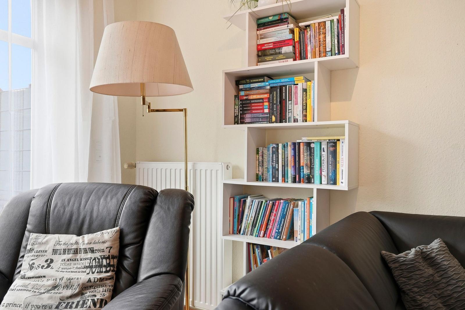 Ein Wohnzimmer mit schwarzen Ledersofas, einem Stehlampe und einem Bücherregal an der Wand.