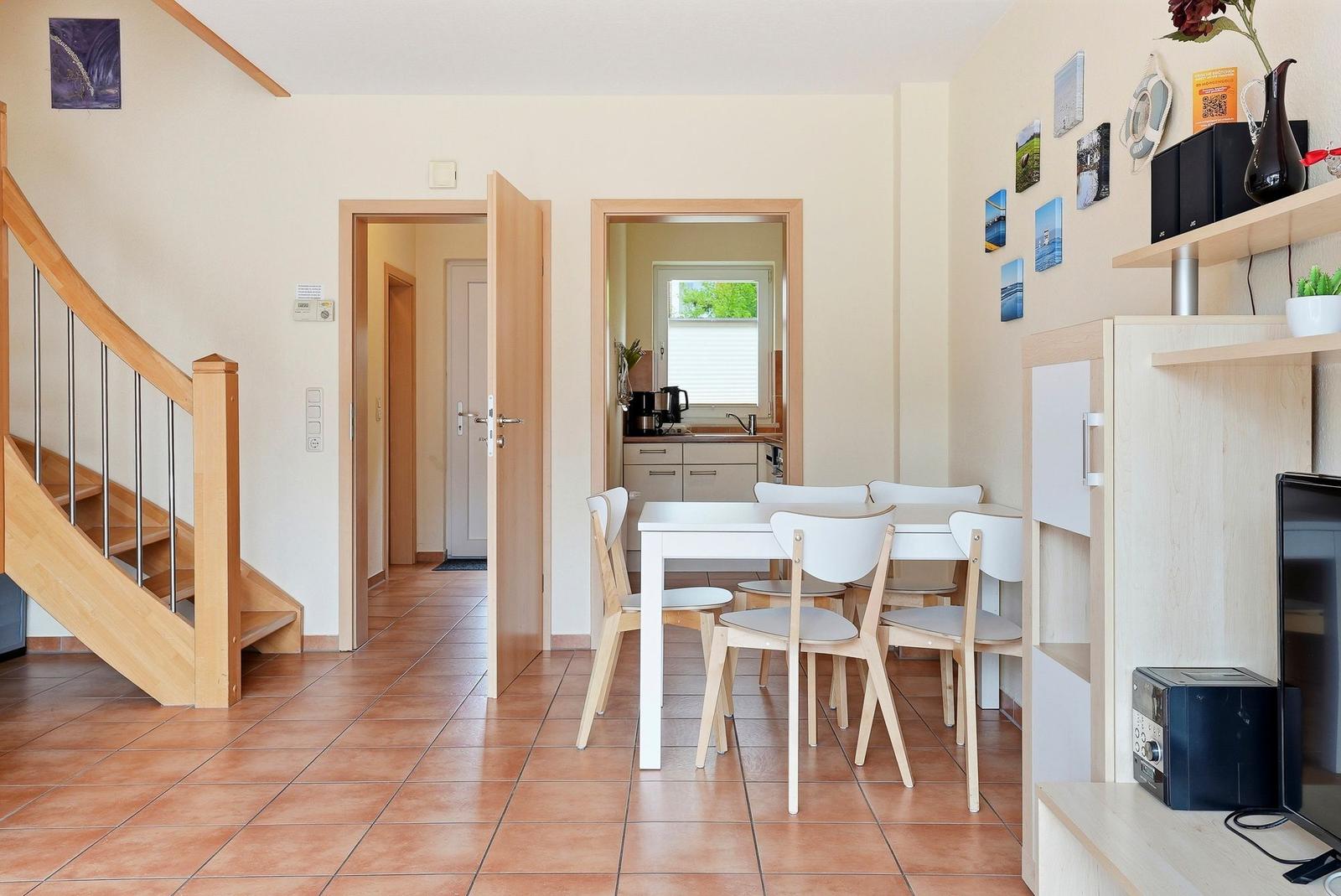 Haus mit Essbereich, Küche und Treppe. Holztreppe, weiße Tische und Stühle.
