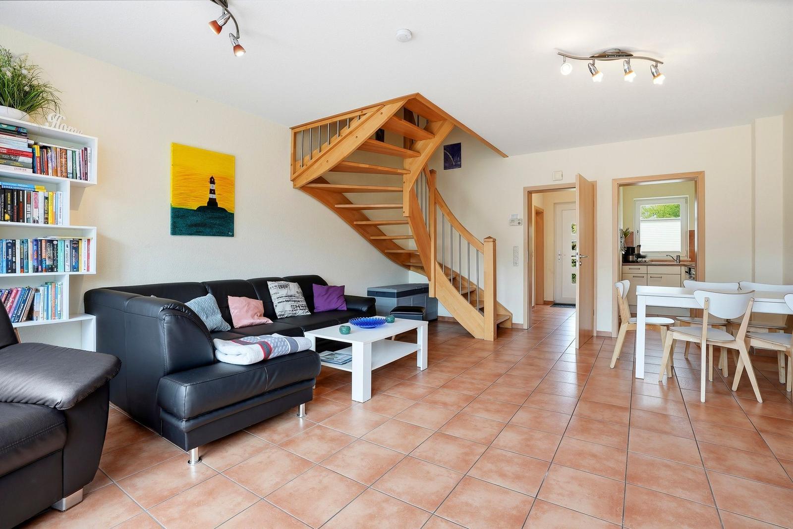 Wohnbereich mit Sofa, Tisch und Holztreppe. Essbereich mit Tisch und Stühlen.