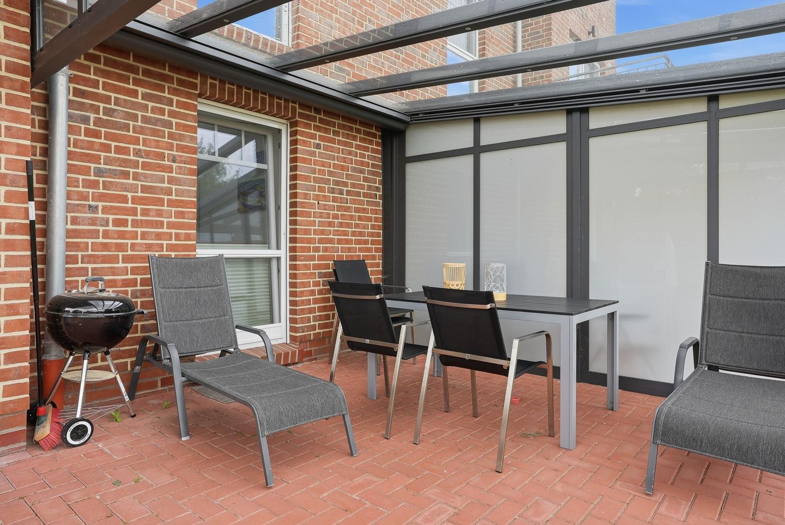 Terrasse mit Grill, Tisch und Stühlen unter Glasdach