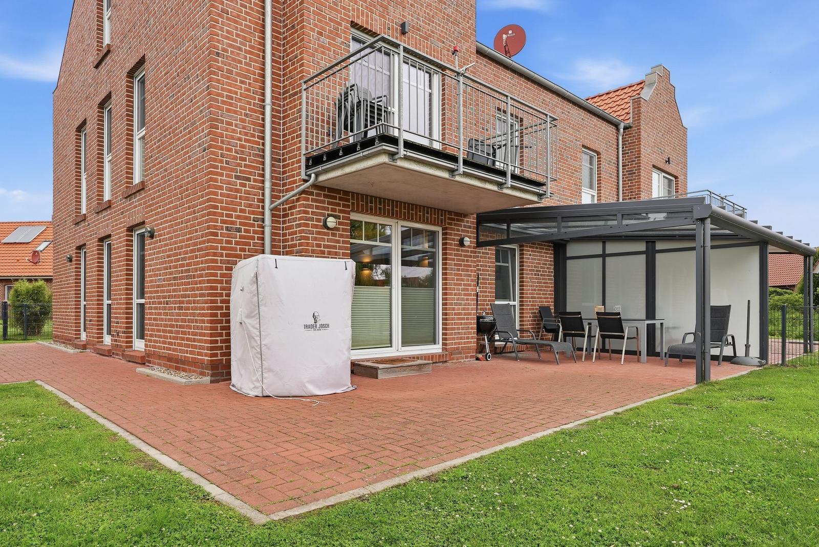 Rotes Backsteingebäude mit Balkon und überdachter Terrasse mit Gartenmöbeln.