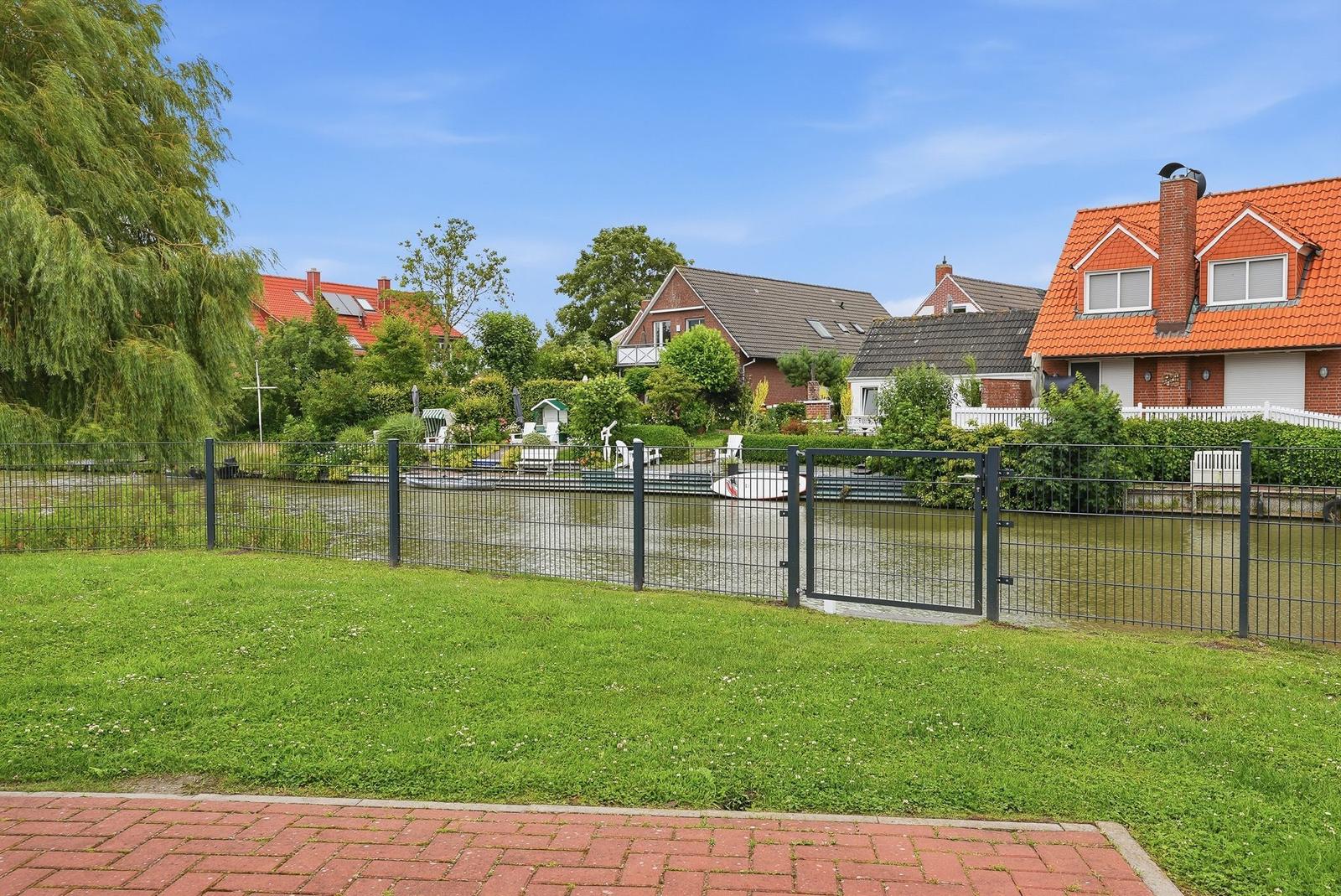 Grüner Rasenbereich neben einem Kanal mit Booten und Häusern im Hintergrund.