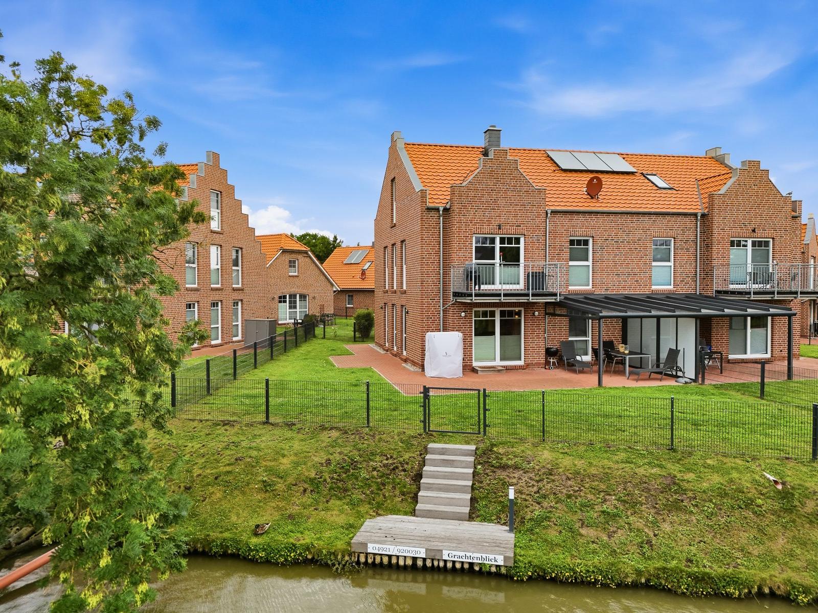 Zwei-stöckige Backsteinhaus mit Terrasse und Garten neben einem Kanal.
