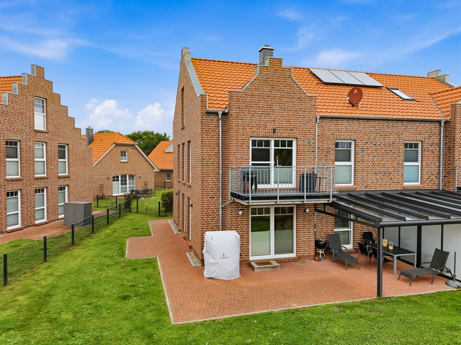 Zweistöckiges Backsteinhaus mit Balkon, Terrasse und Gartenbereich unter klarem Himmel.